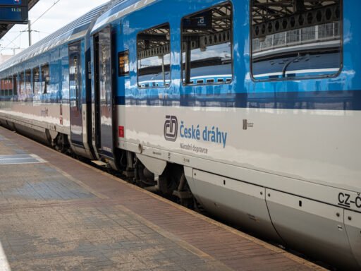 Souprava osobních vozů Českých drah v modrobílém nátěru stojící u nástupiště železniční stanice. Na vozech je viditelné logo národního dopravce