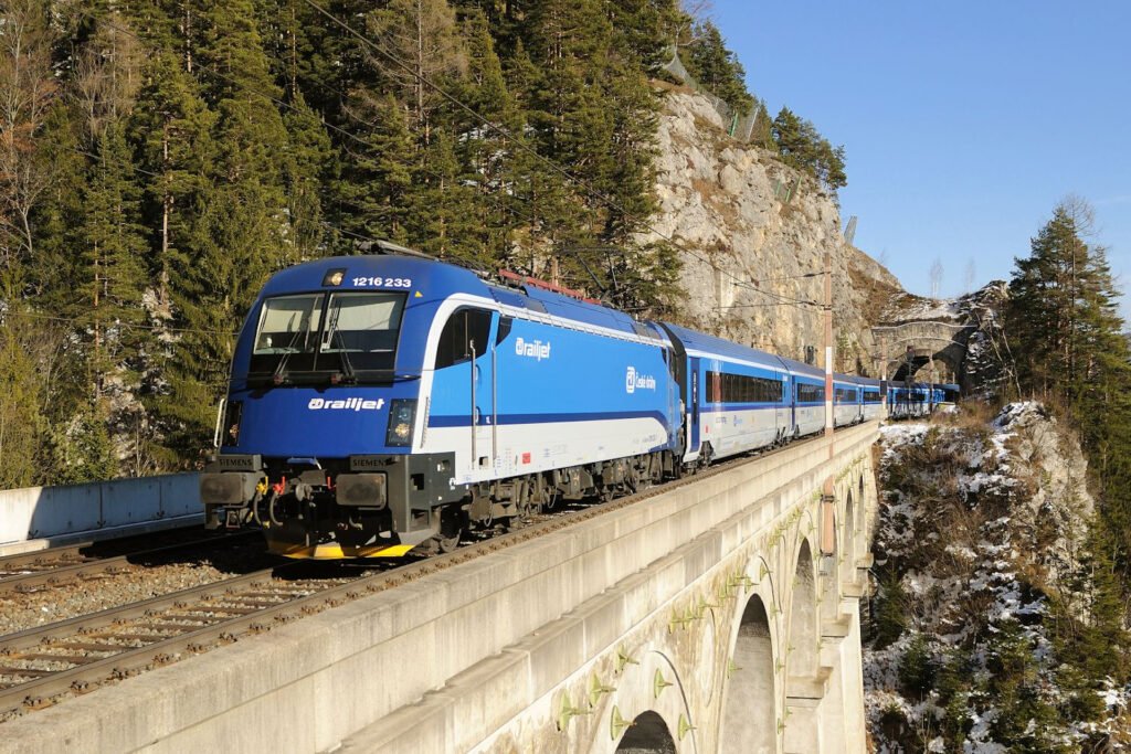 Railjet Českých drah vedený lokomotivou Siemens Taurus 1216 233 projíždí po kamenném železničním viaduktu v horské krajině