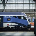 Detail řídicího vozu soupravy railjet Českých drah v modrobílém nátěru na pražském hlavním nádraží, pod historickou prosklenou nádražní halou