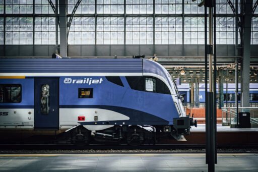 Detail řídicího vozu soupravy railjet Českých drah v modrobílém nátěru na pražském hlavním nádraží, pod historickou prosklenou nádražní halou