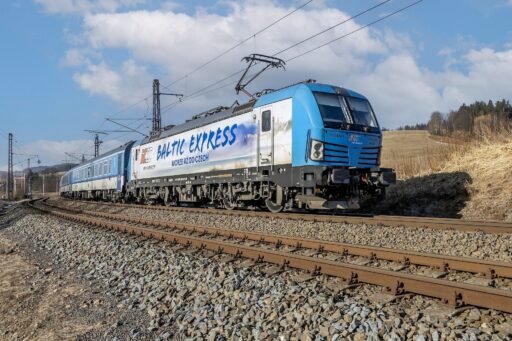 Mezinárodní vlak Baltic Express vedený elektrickou lokomotivou Siemens Vectron v modrobílém nátěru PKP Intercity projíždí po elektrifikované železniční trati v otevřené krajině