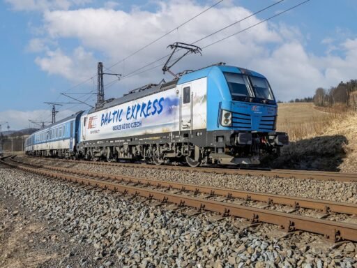 Mezinárodní vlak Baltic Express vedený elektrickou lokomotivou Siemens Vectron v modrobílém nátěru PKP Intercity projíždí po elektrifikované železniční trati v otevřené krajině