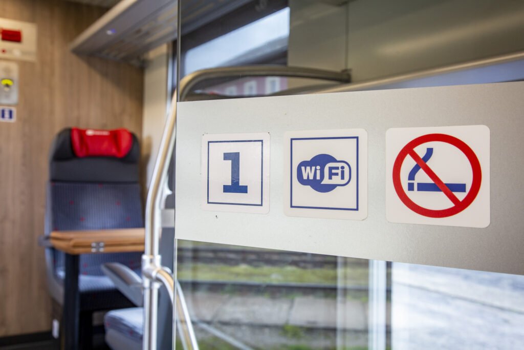 Detail skleněné přepážky v interiéru vozu Českých drah s piktogramy první vozové třídy, dostupné palubní Wi-Fi sítě a zákazu kouření