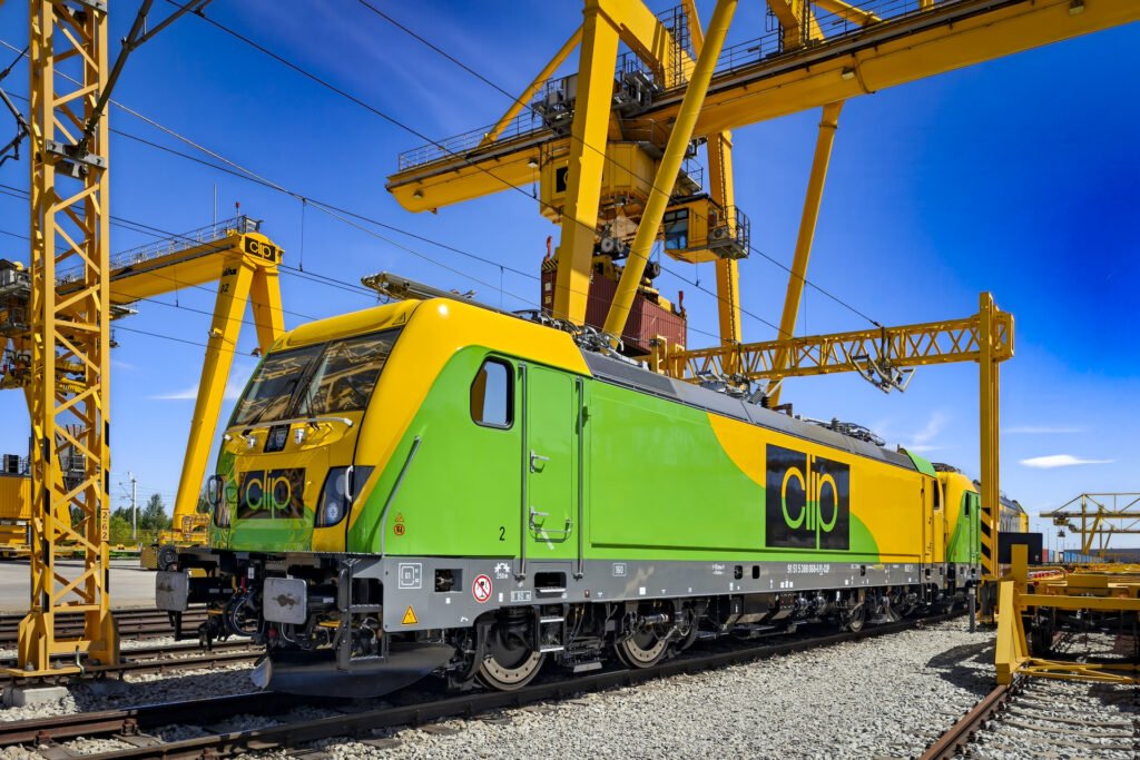 Zelenožlutá elektrická lokomotiva Alstom Traxx Universal polského dopravce CLIP Intermodal v intermodálním terminálu s kontejnerovými jeřáby