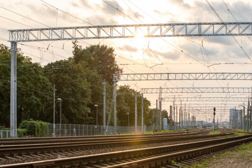 Železniční kolejiště v lotyšské Rize s trakčním vedením při západu slunce. Lotyšsko připravuje nové železniční spojení centra města s mezinárodním letištěm