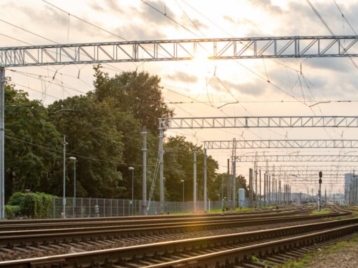 Železniční kolejiště v lotyšské Rize s trakčním vedením při západu slunce. Lotyšsko připravuje nové železniční spojení centra města s mezinárodním letištěm