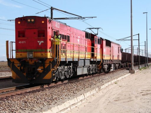 Dieselelektrická lokomotiva řady 43-000 dopravce Transnet Freight Rail v červeném nátěru vede dlouhou soupravu nákladních vozů na železniční trati u jihoafrického města Saldanha